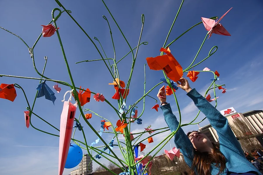 Eine junge Frau befestigt bunte Papierfiguren an einer Kunstinstallation im Freien