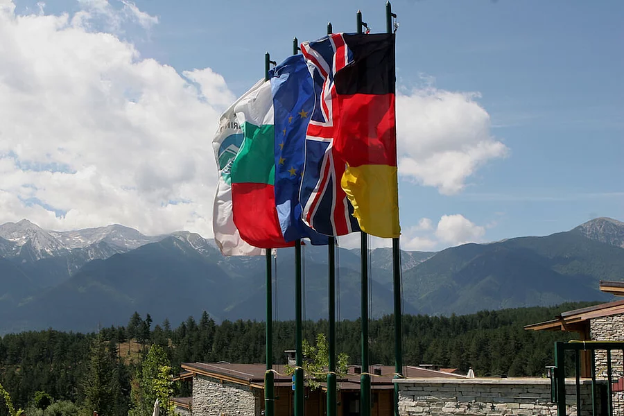 Die Flaggen Bulgariens, der Europäischen Union, des Vereinigten Königreichs und Deutschlands sowie eine Organisationsflagge vor einer Berglandschaft