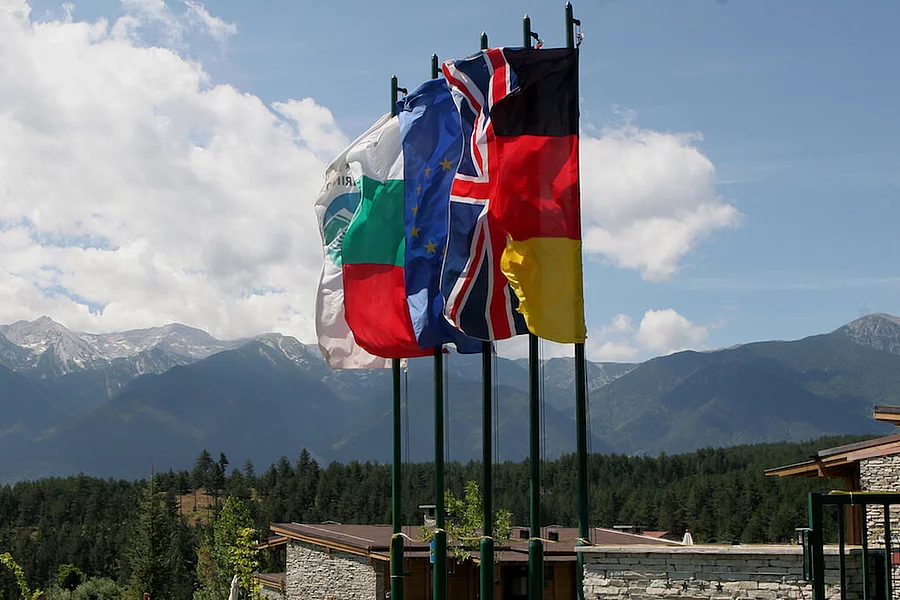 Die Flaggen Bulgariens, der Europäischen Union, des Vereinigten Königreichs und Deutschlands sowie eine Organisationsflagge vor einer Berglandschaft
